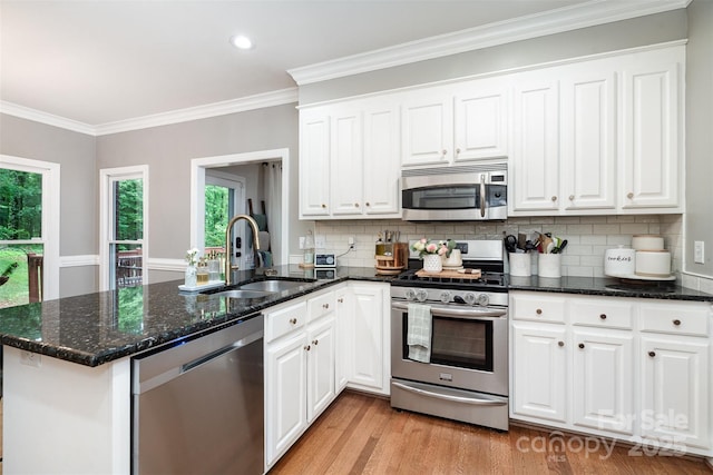 kitchen with stainless steel appliances, a sink, a peninsula, white cabinets, and ornamental molding