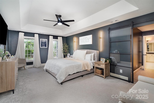 bedroom featuring a tray ceiling, carpet floors, a barn door, and baseboards