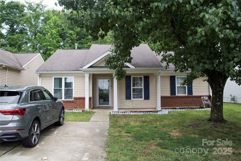 view of front of home featuring brick siding, a front yard, roof with shingles, and covered porch