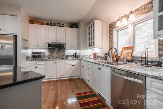kitchen with appliances with stainless steel finishes, a sink, vaulted ceiling, dark wood-type flooring, and white cabinets