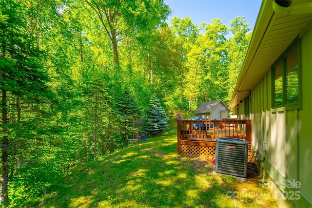 view of green lawn with central air condition unit, a deck, and a view of trees