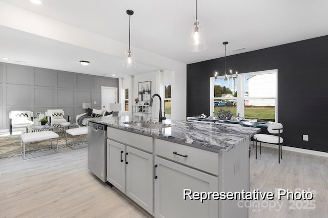 kitchen with a sink, dishwasher, light wood-type flooring, light stone countertops, and a decorative wall