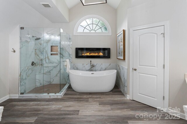 9433 Wallace Pond Dr, Huntersville, NC 28078 - full bath featuring a freestanding tub, a marble finish shower, vaulted ceiling, a glass covered fireplace, and wood finished floors