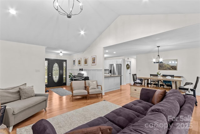 living room featuring a chandelier, light wood finished floors, high vaulted ceiling, and a wainscoted wall