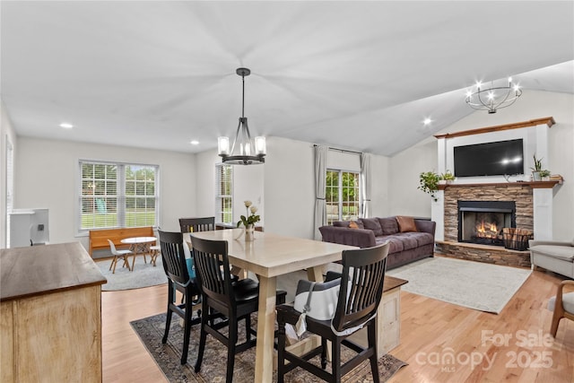 dining space featuring a chandelier, light wood-style flooring, a stone fireplace, vaulted ceiling, and recessed lighting