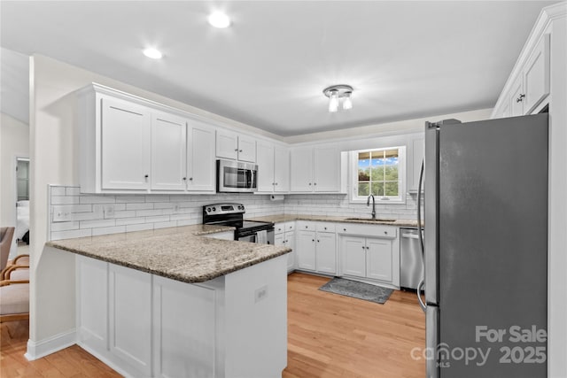 kitchen featuring appliances with stainless steel finishes, a peninsula, a sink, light wood-style floors, and white cabinets