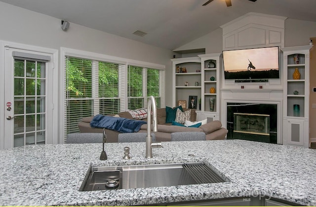 kitchen featuring a sink, a ceiling fan, light stone counters, open floor plan, and lofted ceiling
