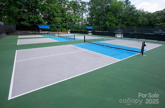 view of tennis court featuring fence, community basketball court, and view of scattered trees