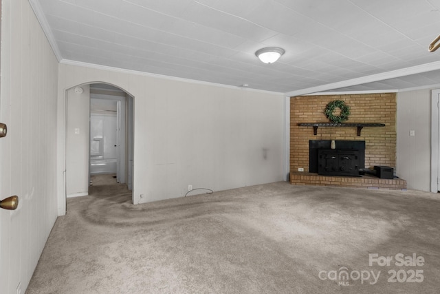 unfurnished living room featuring arched walkways, carpet floors, crown molding, and a brick fireplace