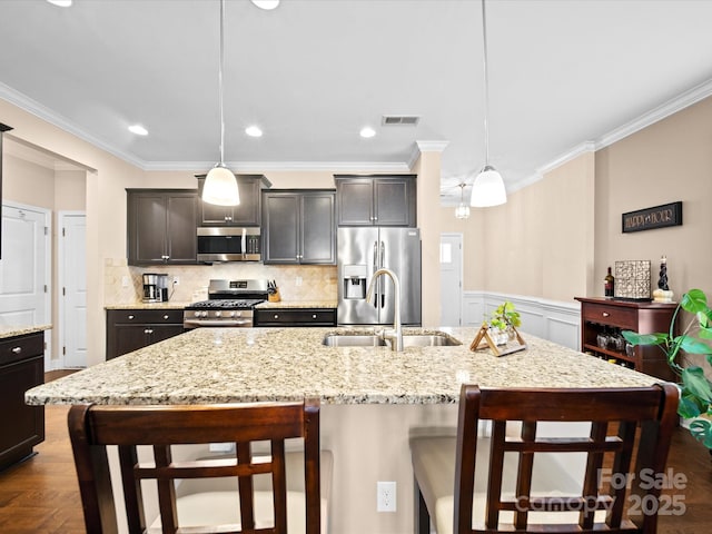 kitchen featuring appliances with stainless steel finishes, a sink, a breakfast bar, ornamental molding, and decorative light fixtures