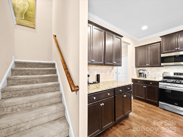 kitchen featuring appliances with stainless steel finishes, dark brown cabinets, ornamental molding, light stone counters, and tasteful backsplash