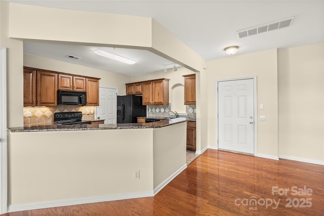 14853 Santa Lucia Dr, Charlotte, NC 28277 - kitchen with black appliances, dark stone counters, a peninsula, tasteful backsplash, and brown cabinets