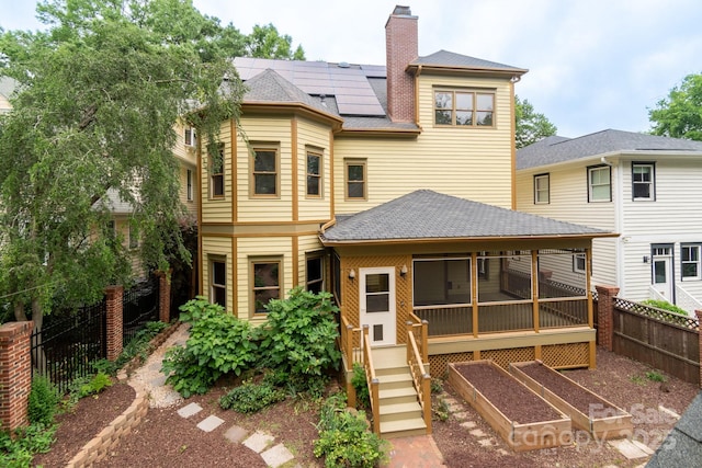 416 E Park Ave, Charlotte, NC 28203 - back of property featuring a sunroom, roof mounted solar panels, a garden, a chimney, and roof with shingles