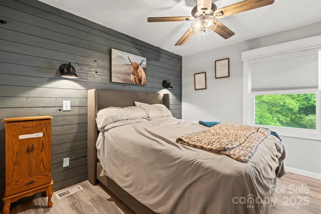 bedroom featuring wooden walls, light wood-type flooring, and ceiling fan