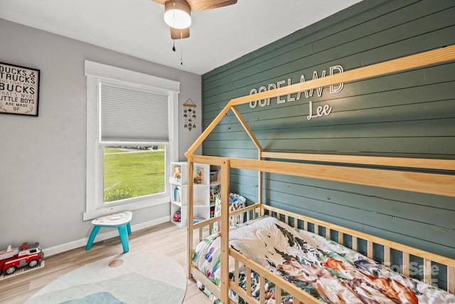 bedroom with wood finished floors, wooden walls, and baseboards