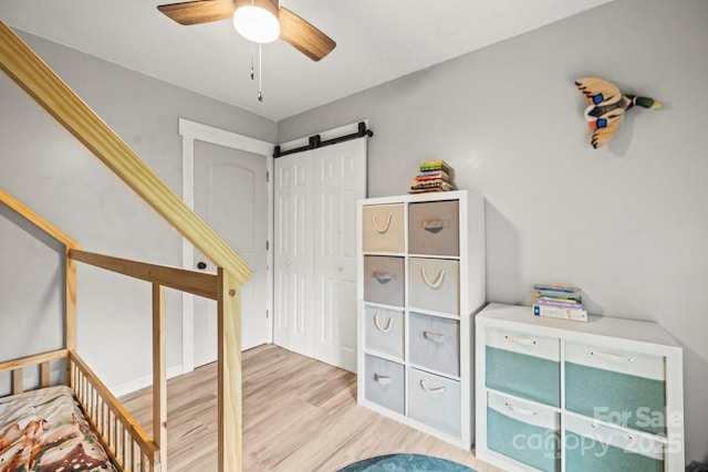 bedroom with a barn door, wood finished floors, and ceiling fan
