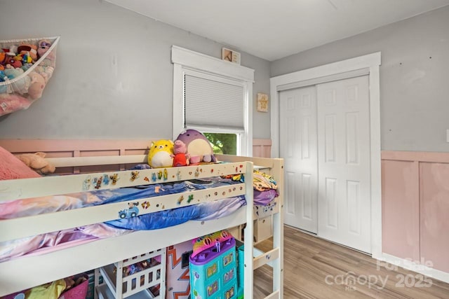bedroom with wood finished floors, a closet, and a wainscoted wall