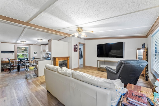 2496 Messer St, Valdese, NC 28690 - living room featuring light wood-type flooring, a textured ceiling, ceiling fan, a glass covered fireplace, and beamed ceiling
