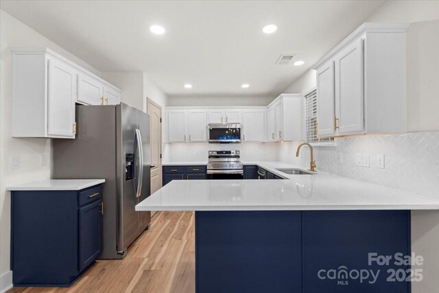 130 Valley Glen Dr, Troutman, NC 28166 - kitchen with stainless steel appliances, a sink, blue cabinetry, light wood-style flooring, and a peninsula