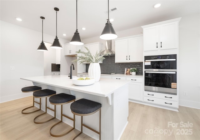 219 Tillery Ln Unit 755, Mount Gilead, NC 27306 - kitchen featuring wall chimney range hood, tasteful backsplash, light wood-type flooring, a center island with sink, and recessed lighting