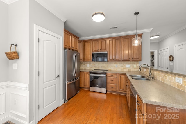516 King St, Waxhaw, NC 28173 - kitchen with appliances with stainless steel finishes, a sink, brown cabinets, crown molding, and a peninsula