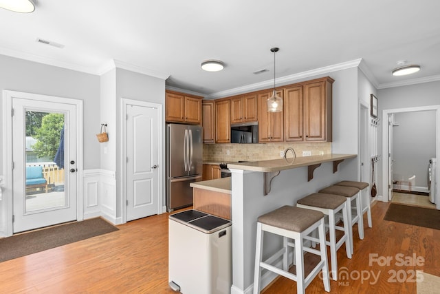 516 King St, Waxhaw, NC 28173 - kitchen with stainless steel appliances, light wood-type flooring, a kitchen bar, a peninsula, and ornamental molding