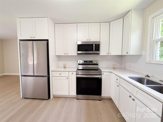 2469 Elkwood Cir, Charlotte, NC 28205 - kitchen with appliances with stainless steel finishes, light wood-style flooring, backsplash, and white cabinets