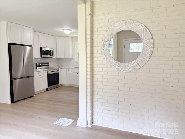 2469 Elkwood Cir, Charlotte, NC 28205 - kitchen featuring stainless steel appliances, light wood-style floors, white cabinetry, light countertops, and brick wall