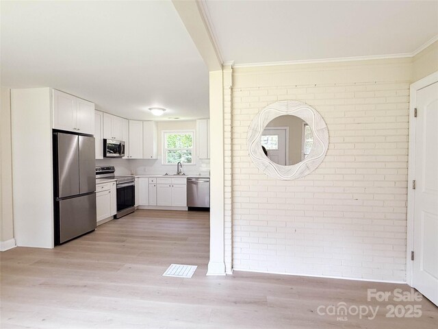 2469 Elkwood Cir, Charlotte, NC 28205 - kitchen featuring appliances with stainless steel finishes, brick wall, a sink, light wood-type flooring, and white cabinetry