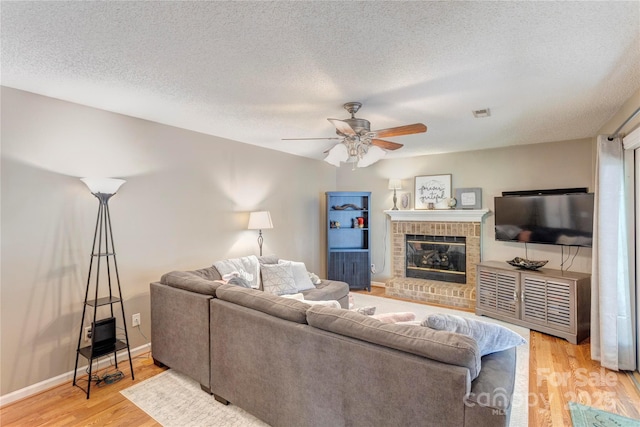 living area with light wood finished floors, ceiling fan, a textured ceiling, a fireplace, and baseboards