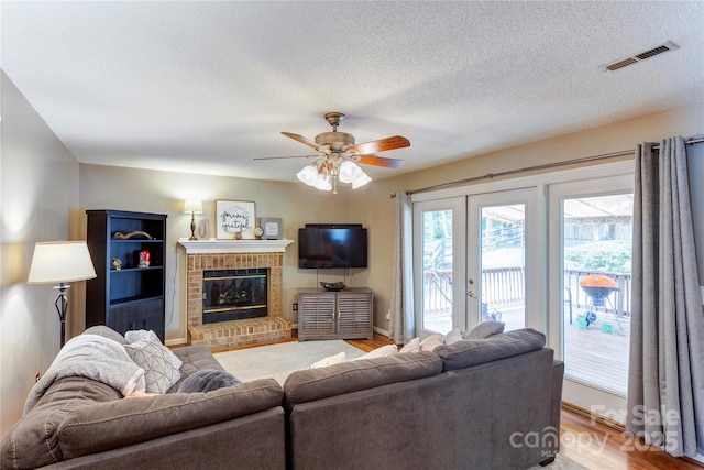 living area featuring light wood-type flooring, french doors, ceiling fan, a brick fireplace, and a textured ceiling