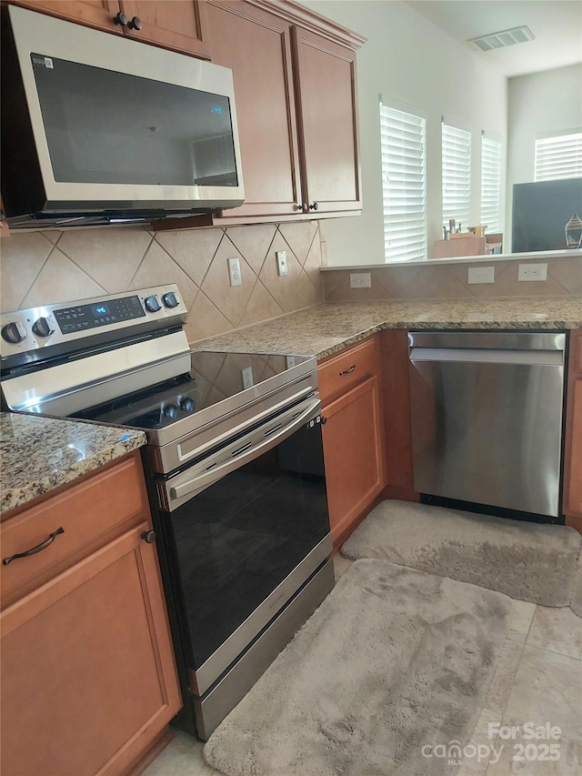 2061 Argentum Ave, Fort Mill, SC 29707 - kitchen with stainless steel appliances, decorative backsplash, brown cabinetry, and light stone countertops