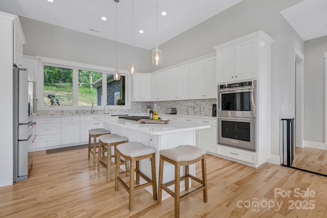 128 Saddle Ridge Dr, Alexander, NC 28701 - kitchen with stainless steel appliances, light wood finished floors, light countertops, backsplash, and a breakfast bar area