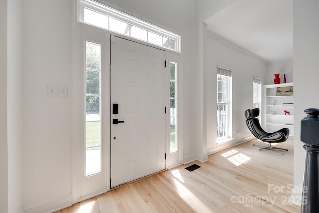 foyer with wood finished floors, ornamental molding, and baseboards