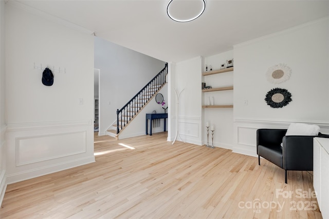 sitting room with wood finished floors, stairway, ornamental molding, and a decorative wall