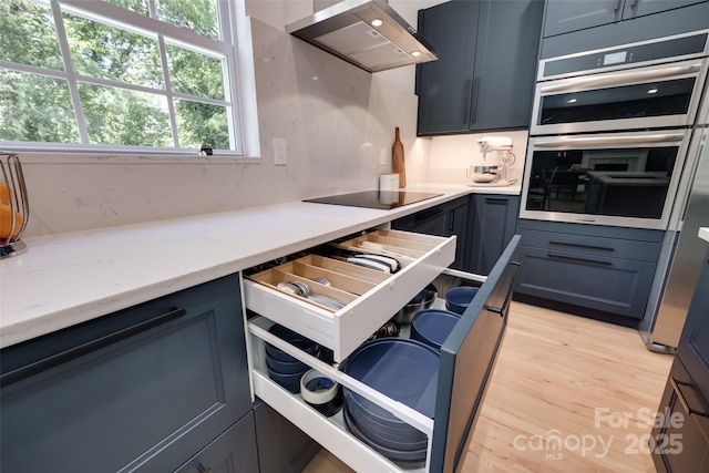 kitchen featuring wall chimney exhaust hood, stainless steel double oven, light wood finished floors, and plenty of natural light