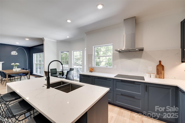 kitchen with wall chimney range hood, ornamental molding, black electric stovetop, a sink, and a breakfast bar area