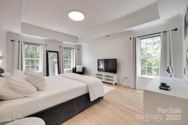 bedroom with a raised ceiling, multiple windows, crown molding, light wood finished floors, and baseboards
