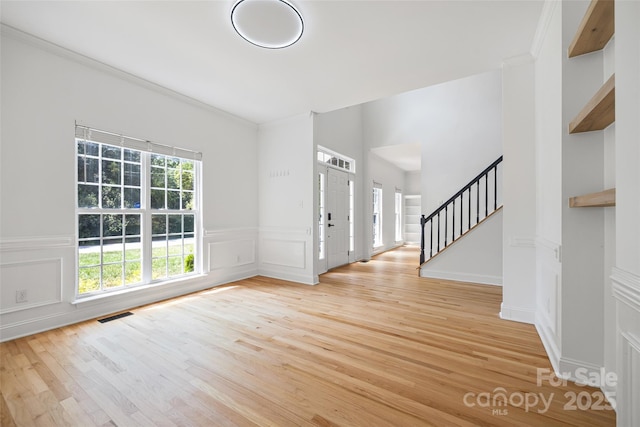 1134 Blueberry Ln, Charlotte, NC 28226 - empty room featuring stairs, light wood-style floors, a wainscoted wall, crown molding, and a decorative wall
