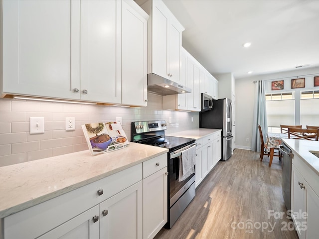 1456 Augustus Beamon Dr, Indian Trail, NC 28079 - kitchen featuring appliances with stainless steel finishes, under cabinet range hood, light wood-type flooring, white cabinetry, and tasteful backsplash