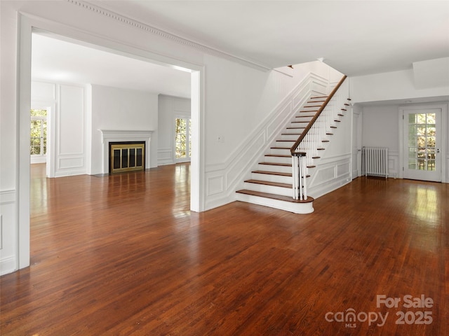 316 Vanderbilt Rd, Asheville, NC 28803 - unfurnished living room featuring radiator, a decorative wall, wood finished floors, stairway, and a fireplace with flush hearth