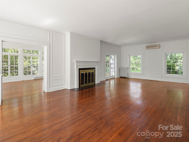 316 Vanderbilt Rd, Asheville, NC 28803 - unfurnished living room with a decorative wall, radiator heating unit, a wall mounted AC, wood finished floors, and a fireplace with flush hearth