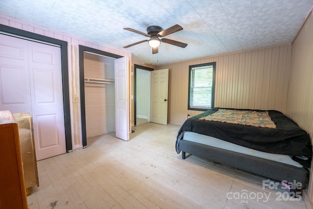 181 Settlers Ln, Waynesville, NC 28785 - bedroom featuring light wood-style floors, multiple closets, wood walls, and a ceiling fan