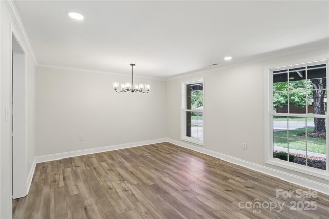 empty room featuring plenty of natural light, a chandelier, wood finished floors, baseboards, and ornamental molding