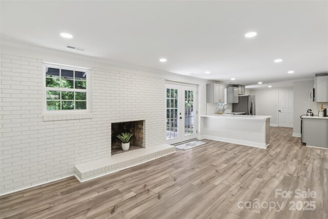unfurnished living room featuring light wood-style flooring, recessed lighting, french doors, a sink, and brick wall