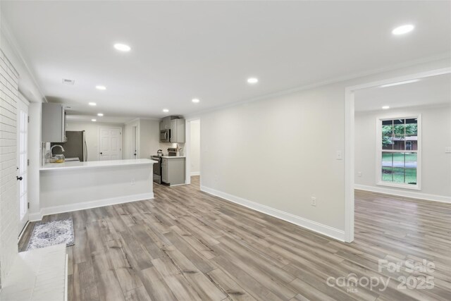 unfurnished living room with recessed lighting, light wood-type flooring, baseboards, and crown molding