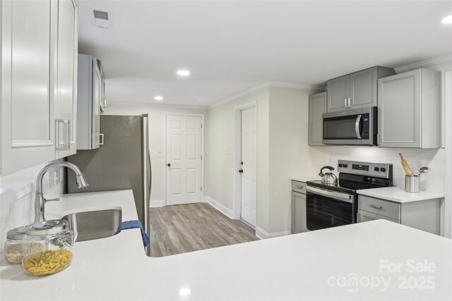 kitchen with appliances with stainless steel finishes, gray cabinets, light wood-style flooring, recessed lighting, and light countertops