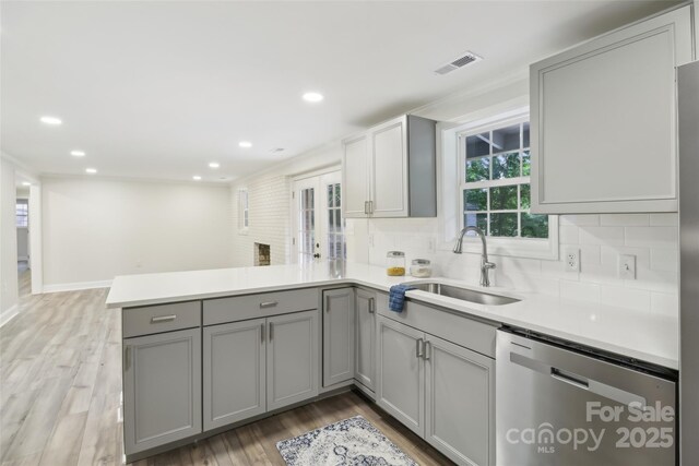 kitchen featuring stainless steel dishwasher, a sink, a peninsula, gray cabinetry, and light wood-style floors
