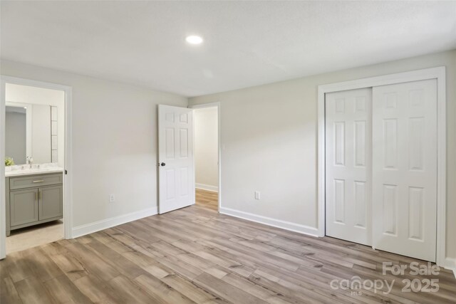 unfurnished bedroom with light wood-style floors, baseboards, a closet, a sink, and recessed lighting
