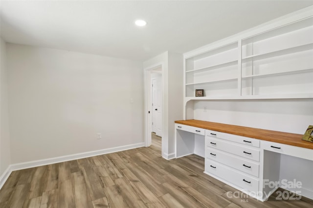 unfurnished office with built in desk, wood finished floors, baseboards, and recessed lighting